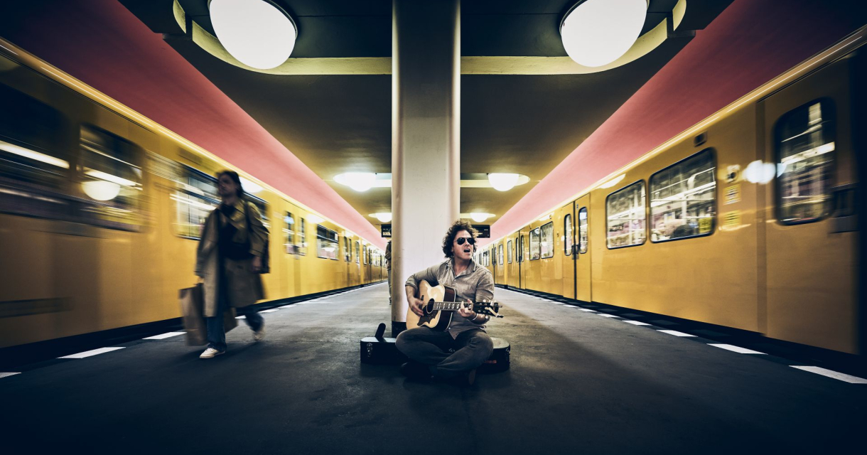 Jasper Steverlinck zittend op een station met een gitaar vast en bewegende metro. Jasper Steverlinck zittend op een station met een gitaar vast en bewegende metro.
