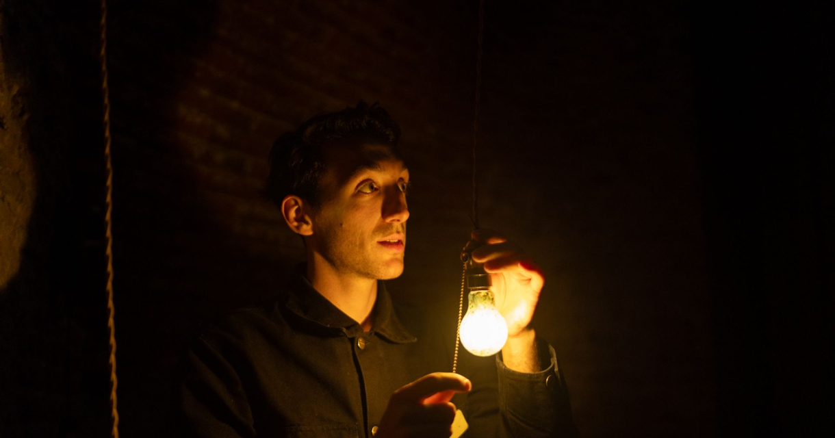 Man in het donker houdt een brandende gloeilamp vast Man in het donker houdt een brandende gloeilamp vast