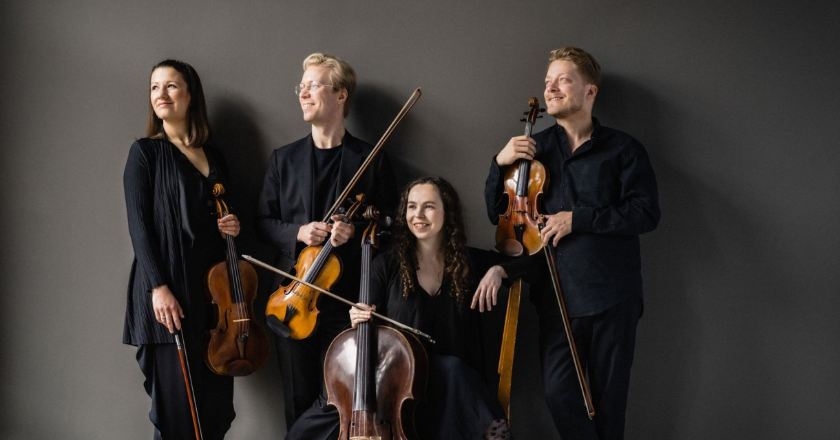 Vier musici in zwarte kleding met strijkinstrumenten poseren ontspannen tegen een grijze muur Vier musici in zwarte kleding met strijkinstrumenten poseren ontspannen tegen een grijze muur