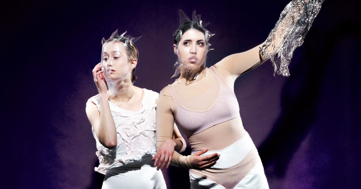 Twee performers in abstracte witte outfits en hoofdstukken poseren expressief tegen een paarse achtergrond Twee performers in abstracte witte outfits en hoofdstukken poseren expressief tegen een paarse achtergrond