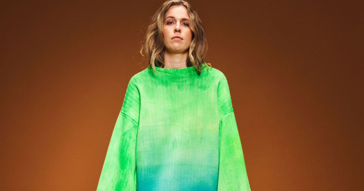 Model in oversized felgroene trui met blauw kleurverloop, poseert voor een effen bruine achtergrond. Model in oversized felgroene trui met blauw kleurverloop, poseert voor een effen bruine achtergrond.