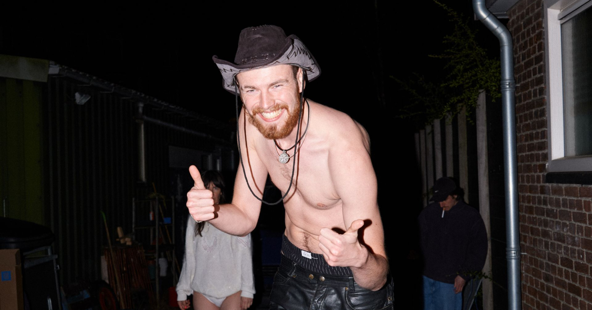 Lachende man met hoed en ontbloot bovenlichaam poseert met duimen omhoog tijdens een avondfeest. Lachende man met hoed en ontbloot bovenlichaam poseert met duimen omhoog tijdens een avondfeest.