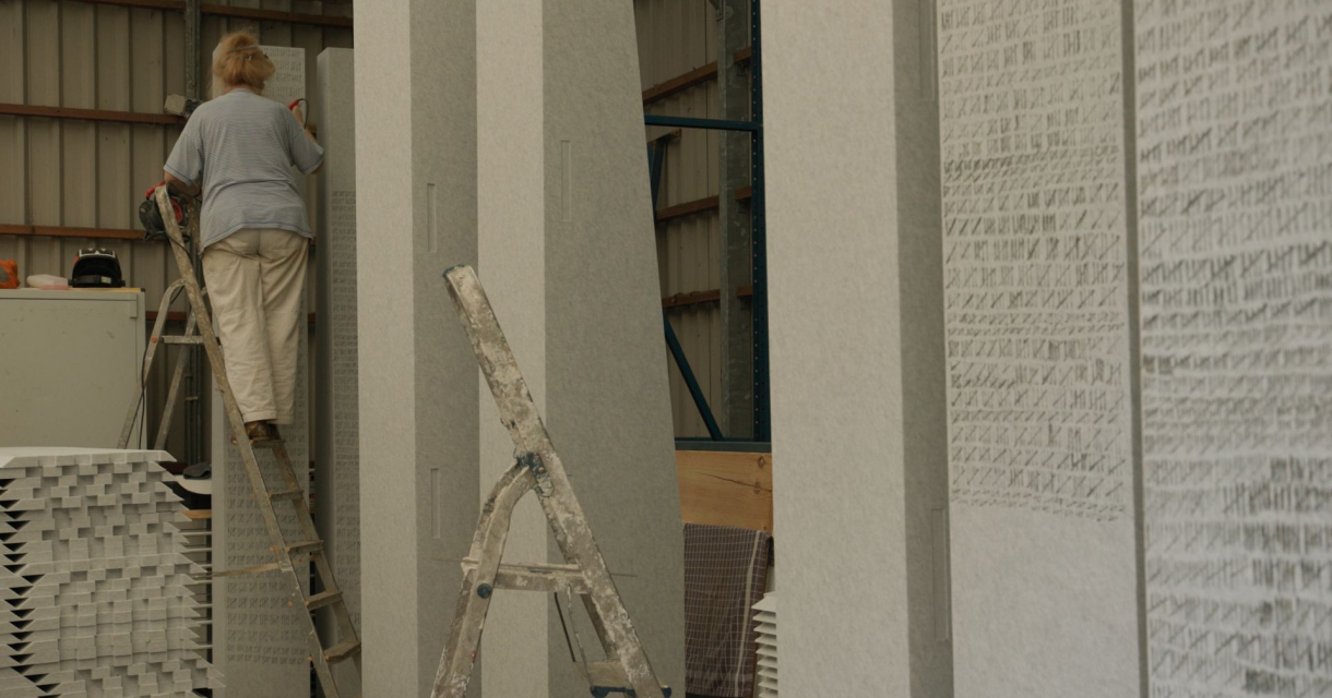 Een vrouw staat op een ijzeren trap naast een beige muur vol met aftelstreepjes