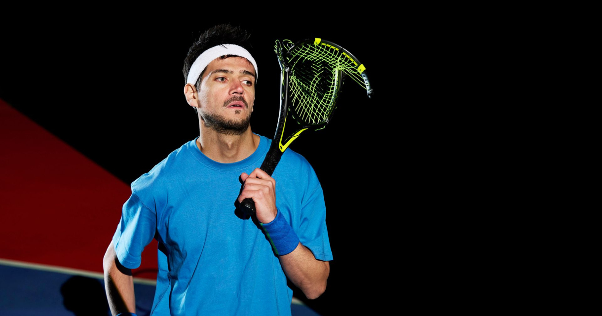 Man in blauw sportshirt met hoofdband en squashracket op een sportveld, zwarte achtergrond. Man in blauw sportshirt met hoofdband en squashracket op een sportveld, zwarte achtergrond.