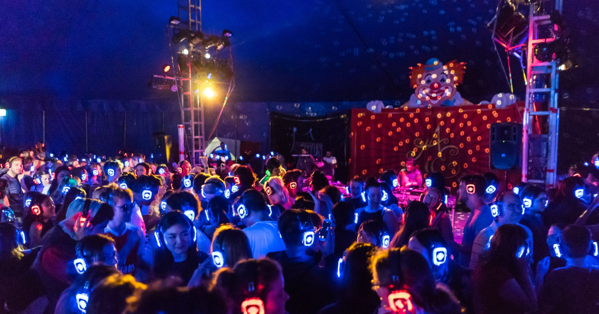 Drukke silent disco met felgekleurde koptelefoons en lichteffecten in een donkere tent Drukke silent disco met felgekleurde koptelefoons en lichteffecten in een donkere tent