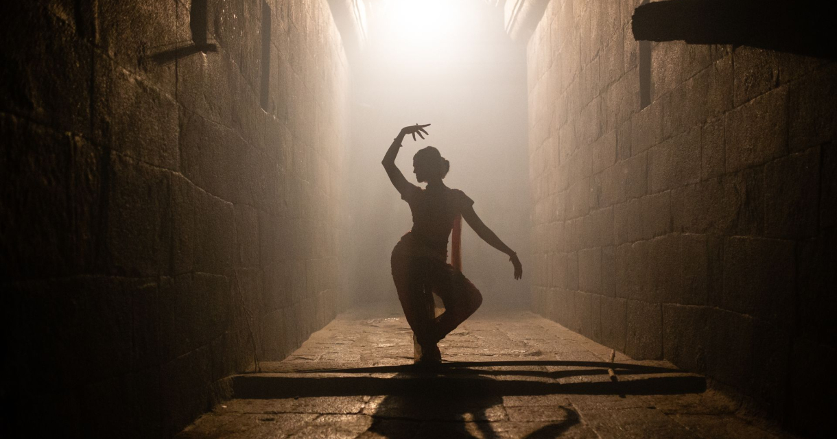 Danseres in ruimte in een moderne pose met lichtinval vanaf achter.