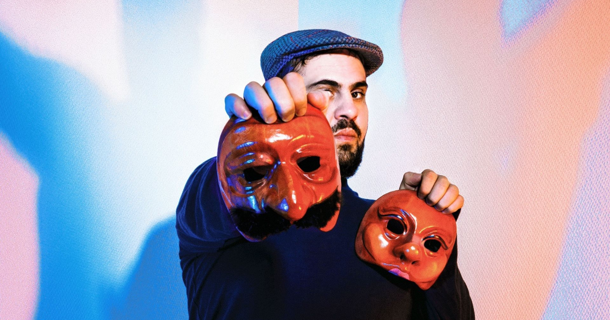 Een man met een pet houdt twee theatrale rode maskers omhoog tegen een kleurrijke achtergrond met blauw en roze licht. Een man met een pet houdt twee theatrale rode maskers omhoog tegen een kleurrijke achtergrond met blauw en roze licht.