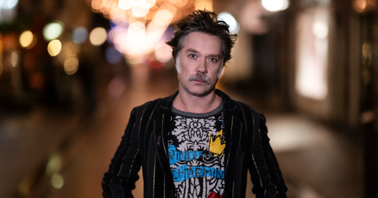 Man poseert zelfverzekerd in een sfeervol verlichte winkelstraat met onscherpe lichtjes op de achtergrond. Man poseert zelfverzekerd in een sfeervol verlichte winkelstraat met onscherpe lichtjes op de achtergrond.