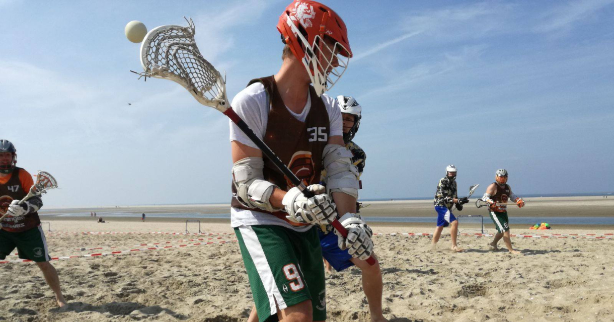 Lacrossewedstrijd op het strand met meerdere spelers in actie, bal zweeft in de lucht, zee en blauwe lucht op de achtergrond Lacrossewedstrijd op het strand met meerdere spelers in actie, bal zweeft in de lucht, zee en blauwe lucht op de achtergrond
