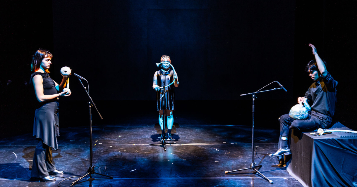 Drie performers op een donker podium met microfoons Drie performers op een donker podium met microfoons