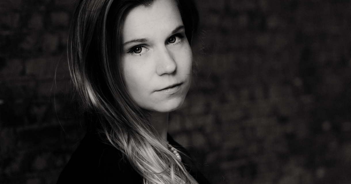 Zwart-witportret van een vrouw met lang haar die serieus in de camera kijkt, staand tegen een bakstenen muur. Zwart-witportret van een vrouw met lang haar die serieus in de camera kijkt, staand tegen een bakstenen muur.