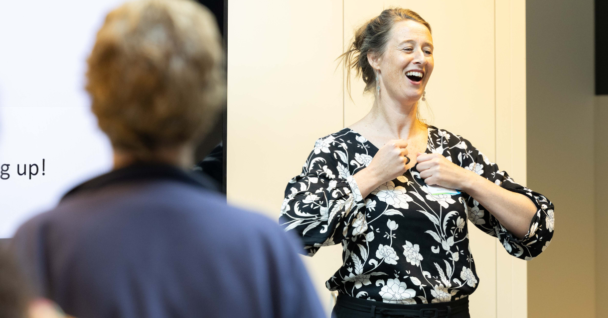 Vrouw met een bloemenblouse geeft enthousiast een presentatie of workshop, terwijl een deelnemer op de voorgrond toekijkt. Vrouw met een bloemenblouse geeft enthousiast een presentatie of workshop, terwijl een deelnemer op de voorgrond toekijkt.