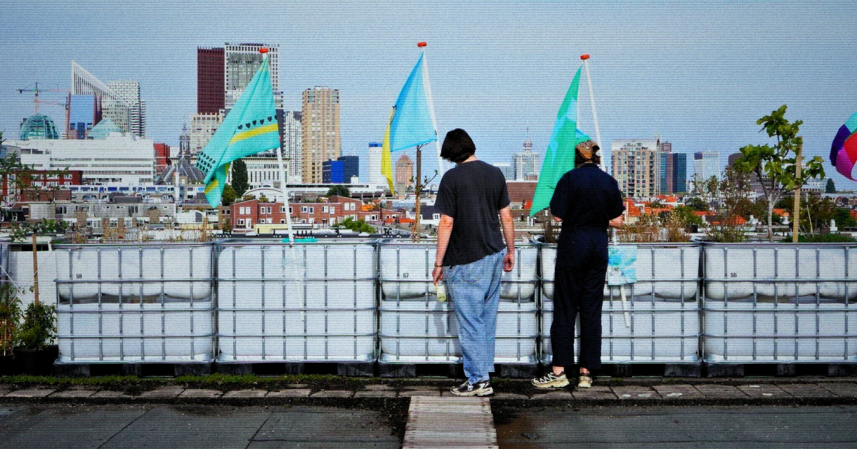Twee mensen kijken uit over de skyline van Den Haag vanaf het creatief ingerichte dakterras met vlaggen van de Energiekas