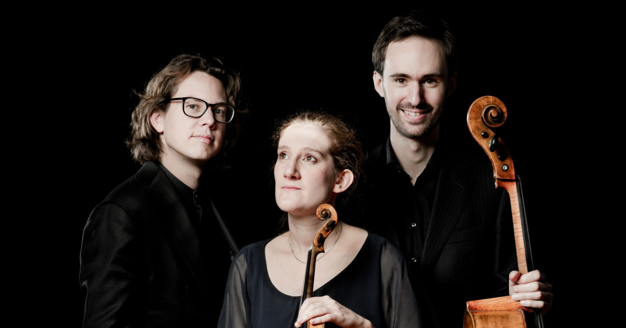 Drie musici poseren met strijkinstrumenten tegen zwarte achtergrond, twee met cello en één met viool in het midden Drie musici poseren met strijkinstrumenten tegen zwarte achtergrond, twee met cello en één met viool in het midden