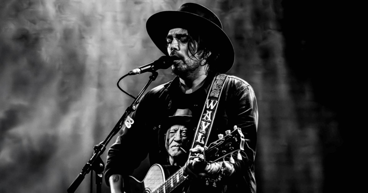 Zanger Waylon met gitaar en hoed zingt in microfoon tijdens liveoptreden Zanger Waylon met gitaar en hoed zingt in microfoon tijdens liveoptreden
