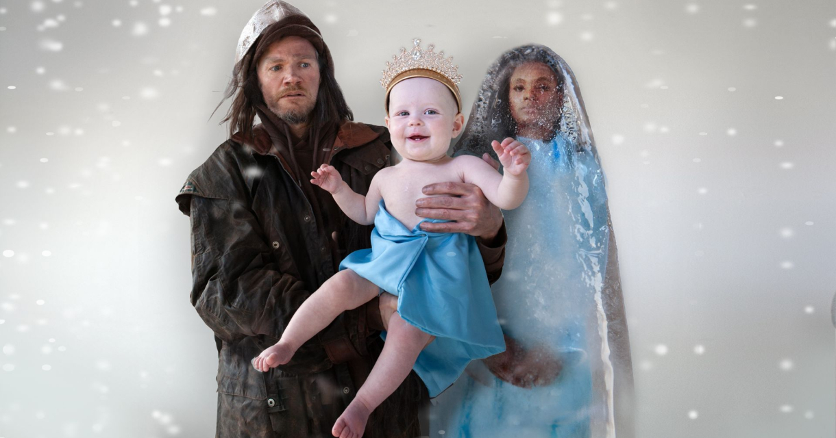 Man en vrouw in winterse kleding houden baby met blauwe doek en kroon vast in vallende sneeuw.
