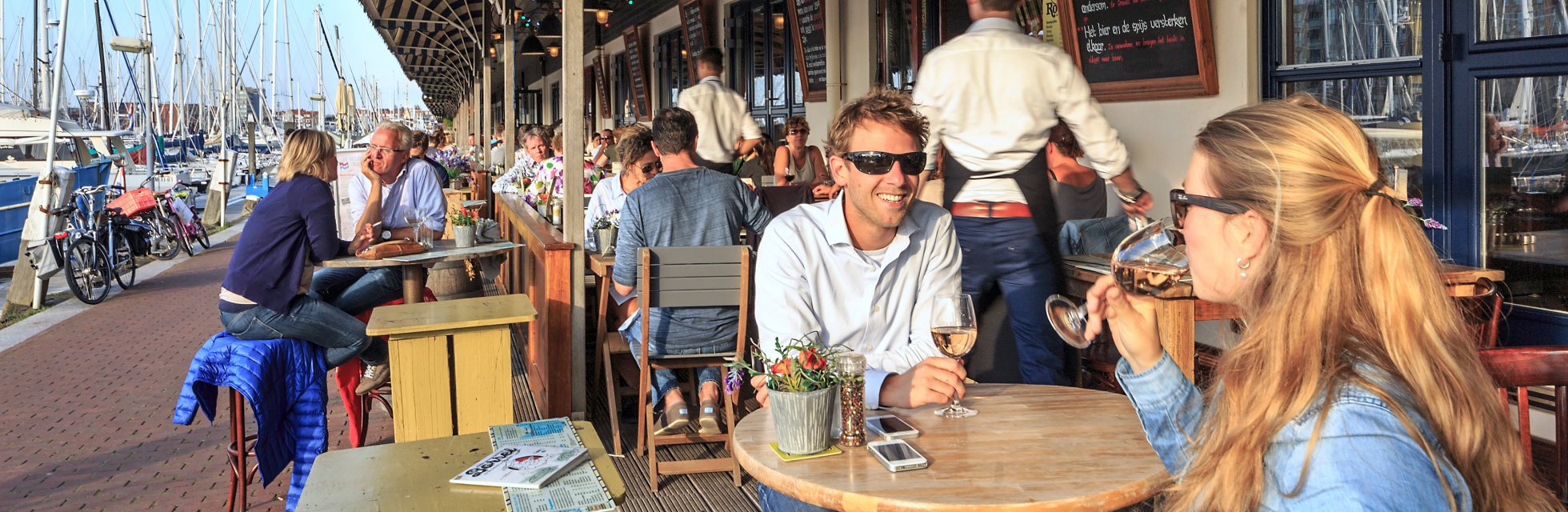 Zicht op restaurants en en mensen die een drankje drinken op terrassen langs de haven van Scheveningen op een zonnige dag