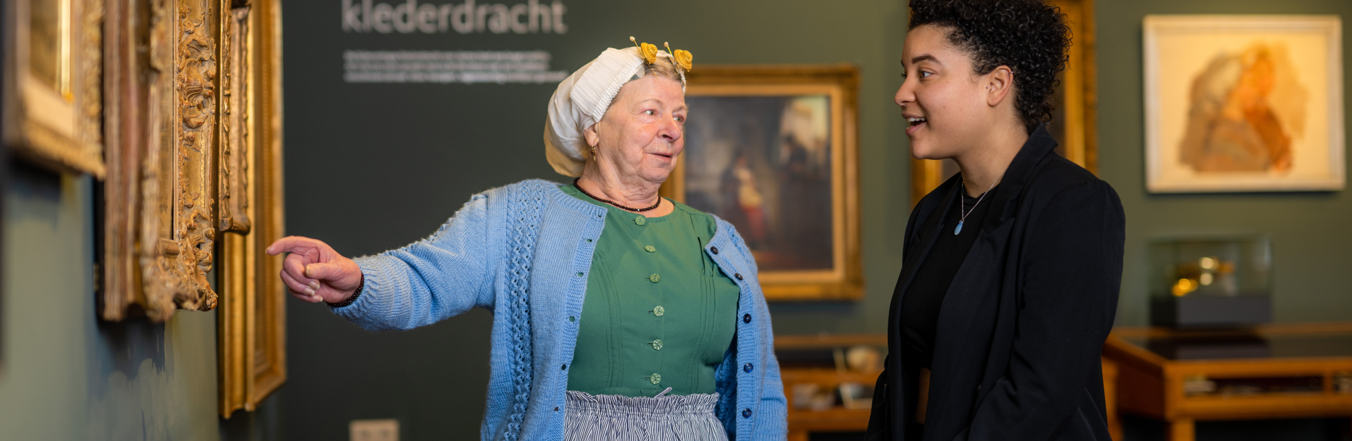 Vrouw in klederdracht wijst iets aan op een schilderij in Muzee Scheveningen