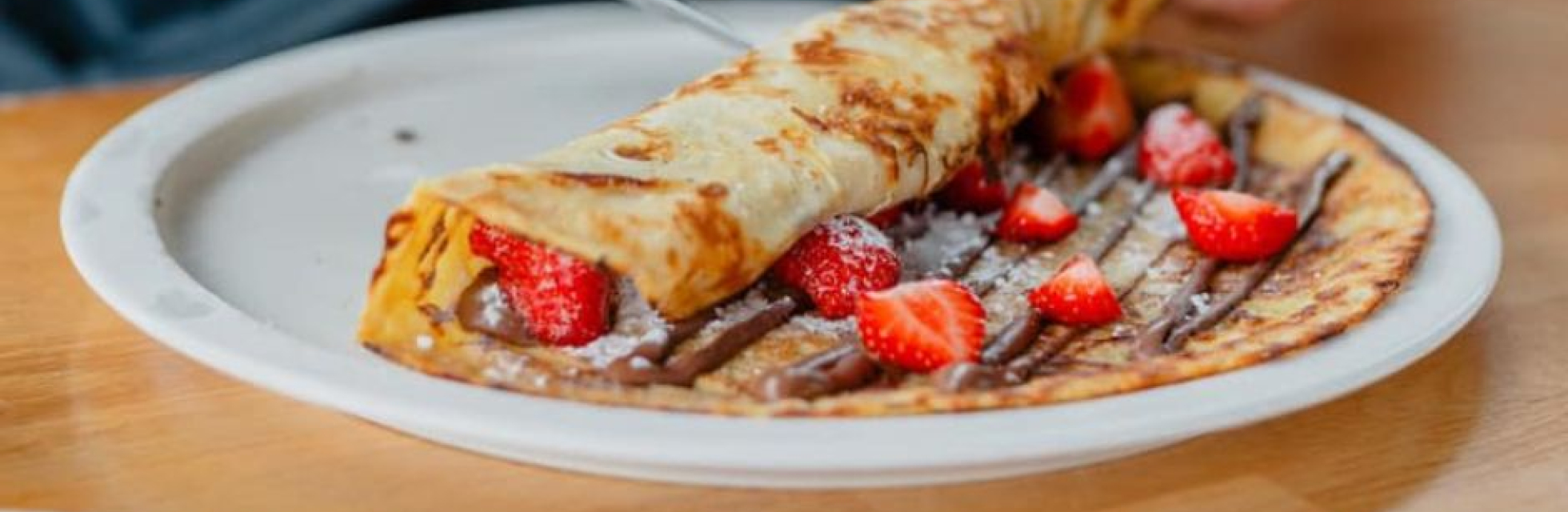 Pannenkoek met nutella en aardbeien en poedersuiker opgerolt.