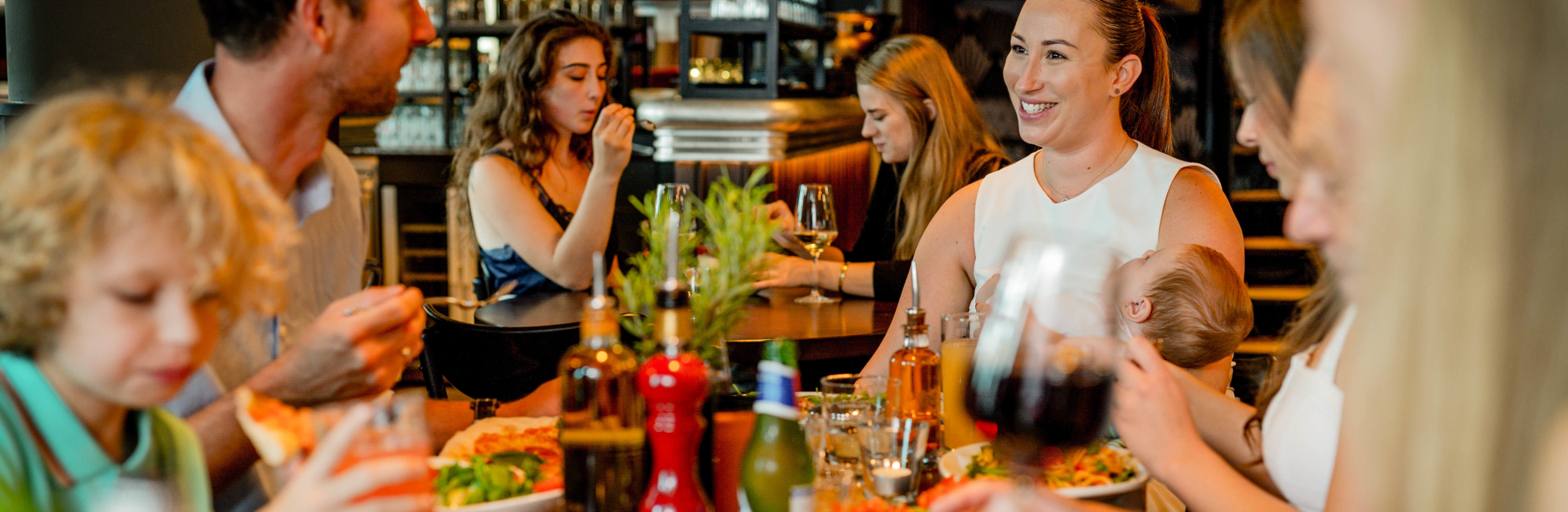 Gezellige familiescène in een restaurant waar mensen genieten van verse pizza en elkaars gezelschap. Een warme, ontspannen sfeer met lachende gezichten.