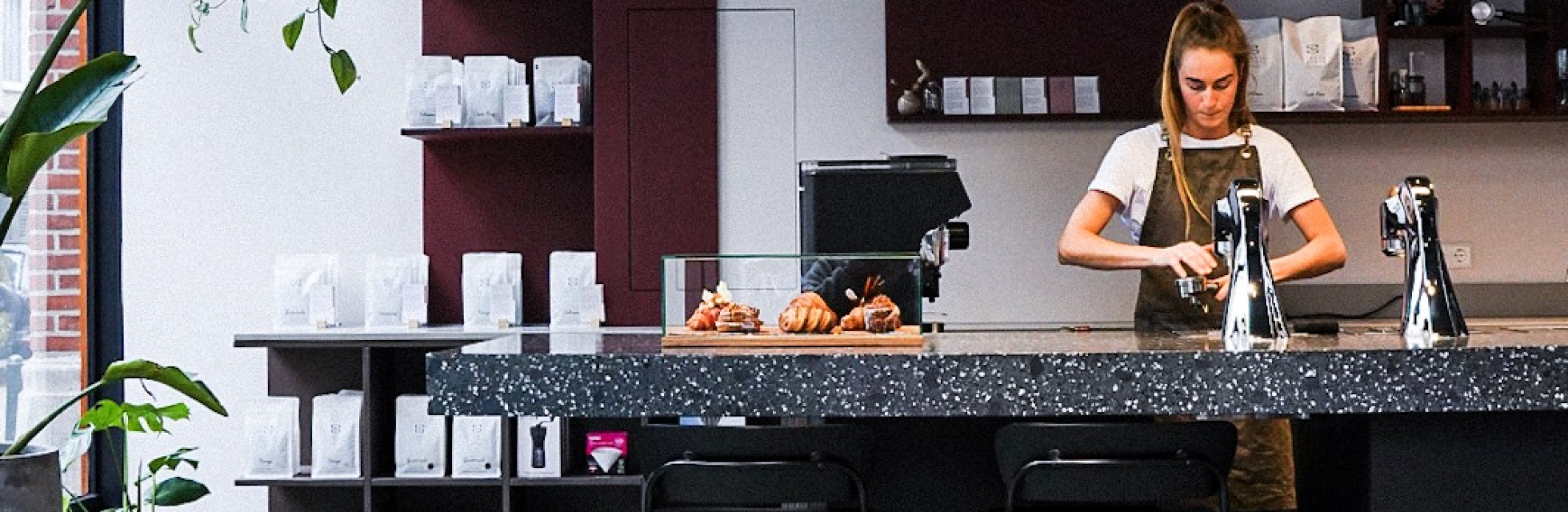 Barista met schort aan het werk in een moderne koffiebar.