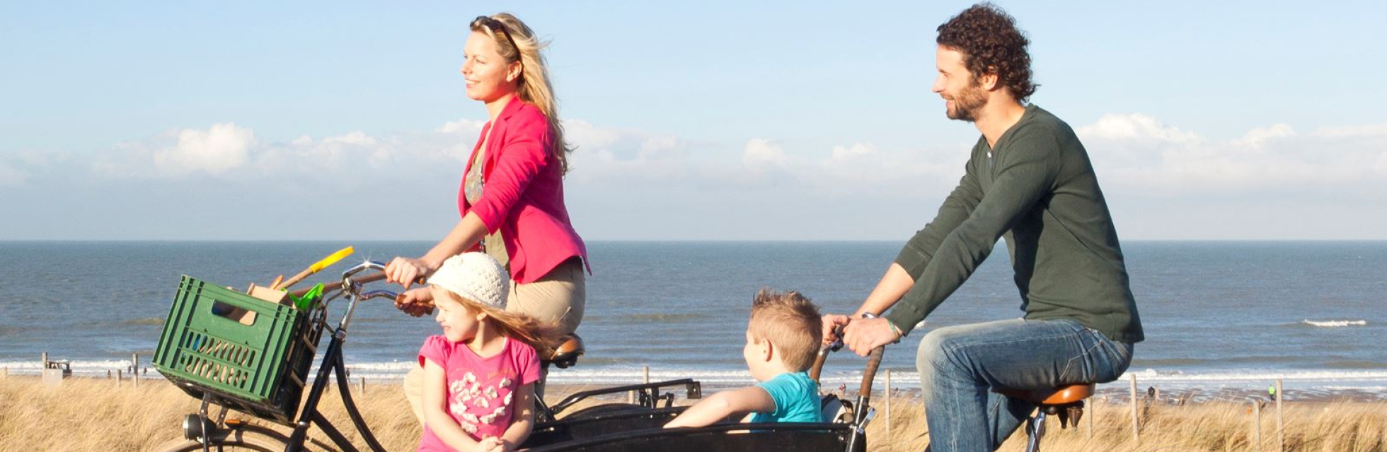 Fietsend stel met kinderen in de bakfiets in de duinen 