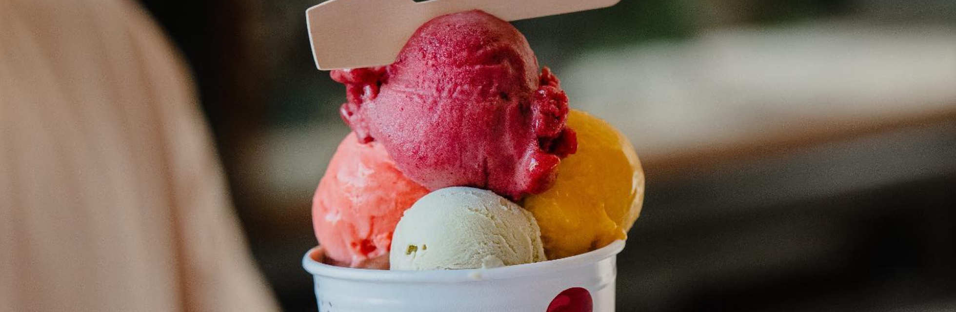 Hand die een bakje ijs van Hop & Stork aanpakt met veel gekleurde bolletjes ijs erin.
