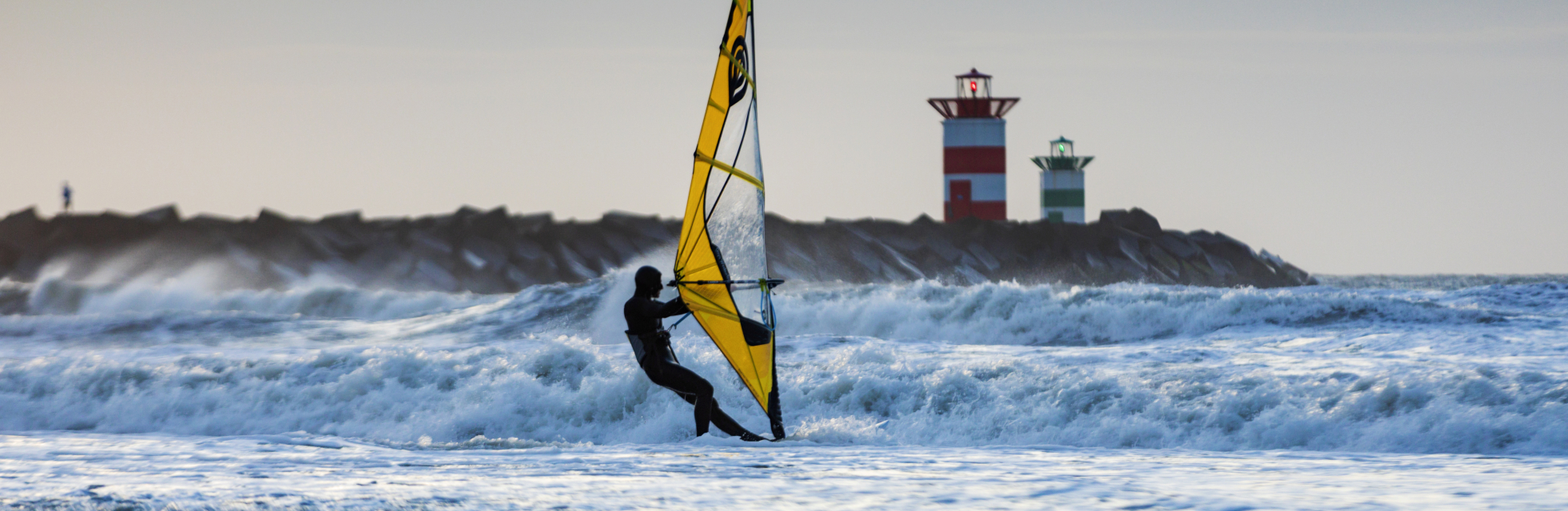 Surfer in zee bij Scheveningen bij het Noordelijk Havenhoofd met het rode havenlicht op de achtergrond. 