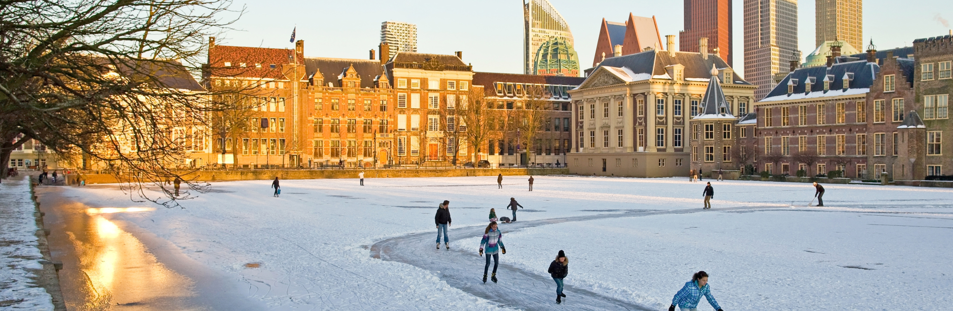 Mensen aan het schaatsen op de bevroren Hofvijver in Den Haag met de moderne skyline op de achtergrond
