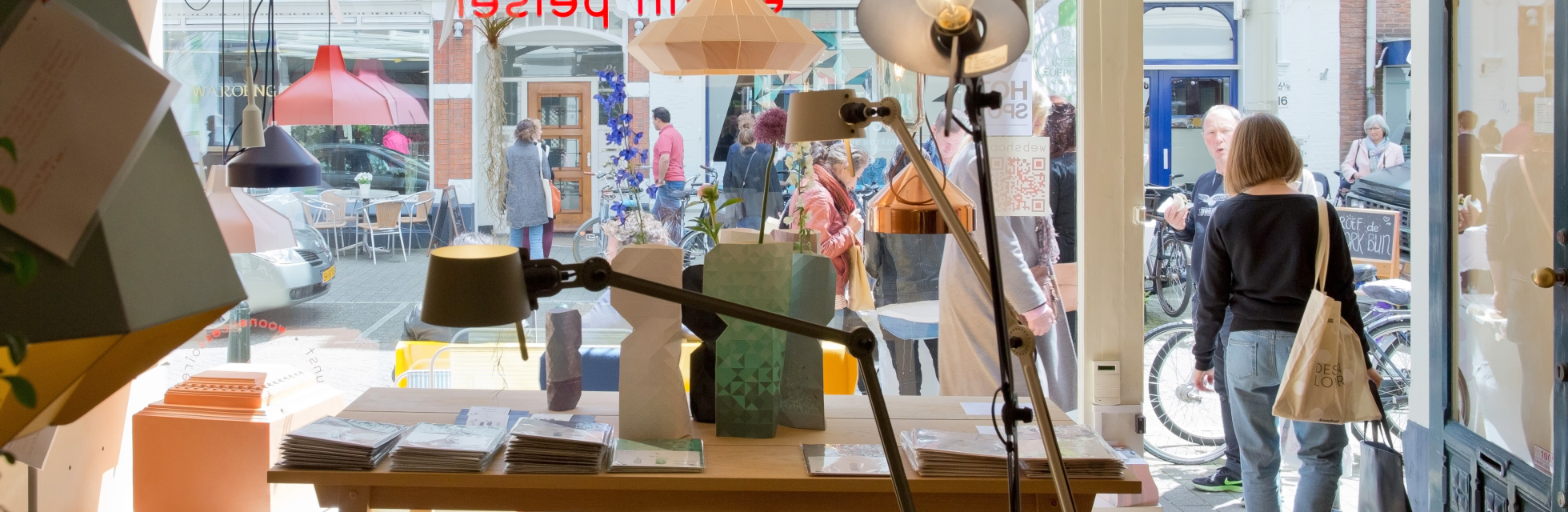 Een blik op een winkelinterieur met lampen en mensen buiten.