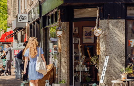 Vrouw loopt door een straat langs een open winkel.