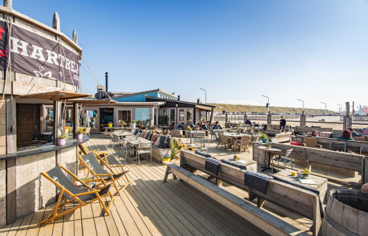 Zonnige terras van Hart Beach met ligstoelen en houten tafels