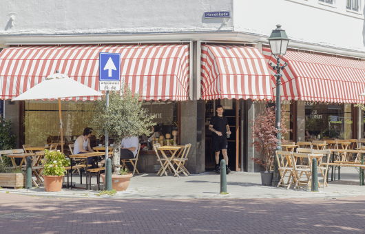 Zomerterrassen bij een café met rode strepen parasols.