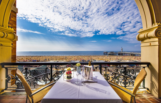 Tafel met macarons en champagne op een balkon met uitzicht op de zee en de Pier van Scheveningen