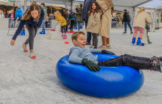 A child slides in a blue ring on the ice rink.