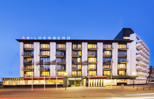Foto van de voorkant van het hotel in de schemer met lichten aan. 