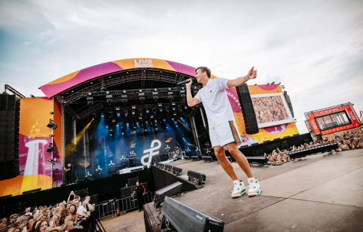 Sänger mit Mikrofon auf der Bühne vor einem Publikum während eines Festivals.