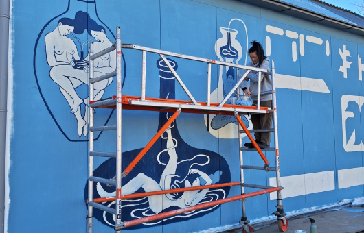 Een vrouw schildert een muurschildering met blauwe achtergronden.