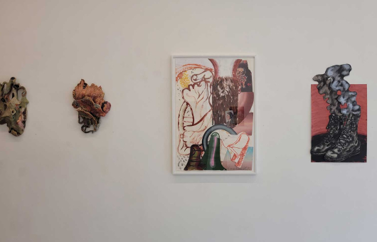 Drie kunstwerken aan een witte muur, waaronder een ingelijste afbeelding.