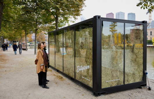 Twee mensen kijken naar een glazen installatie met hooi.