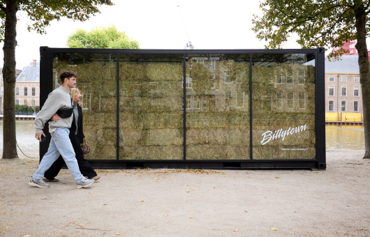 Twee mensen lopen langs een glazen constructie met hooi.