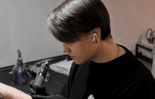 A tattoo artist is tattooing an arm with a machine.