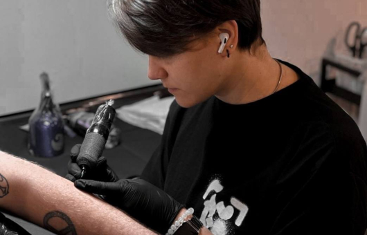 A tattoo artist is tattooing an arm with a tattoo machine.
