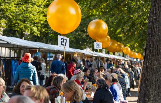 Een drukke markt met mensen en gele ballonnen in Den Haag.