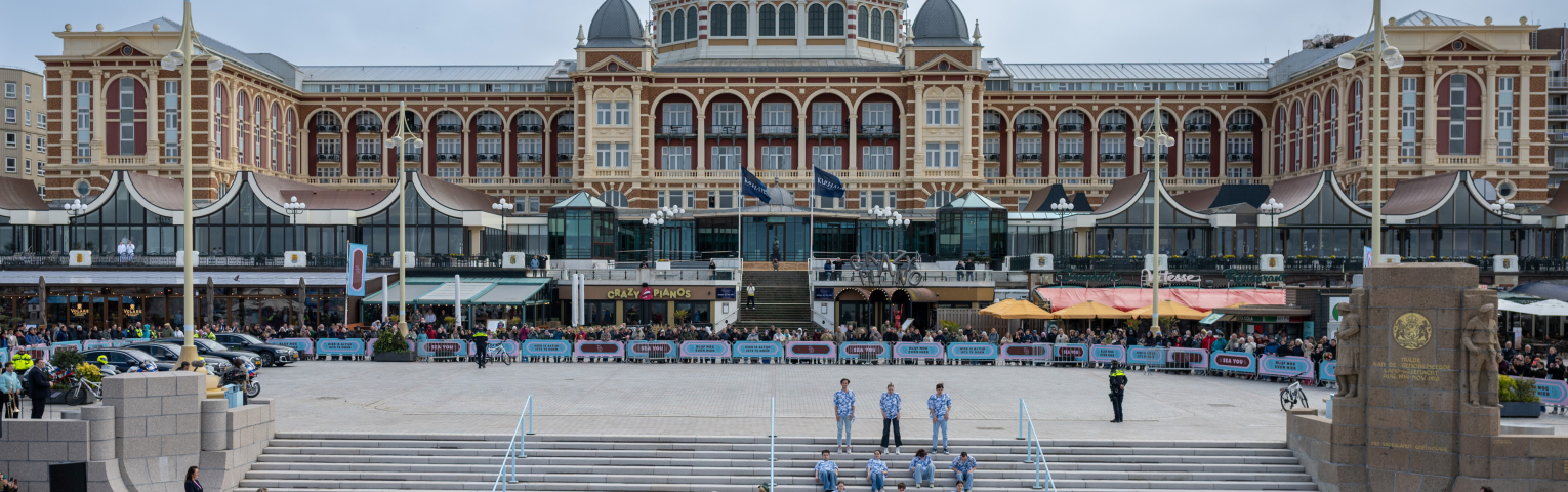 Mensen verzamelen zich voor een evenement bij de Pier, met de achterliggende gebouwen.