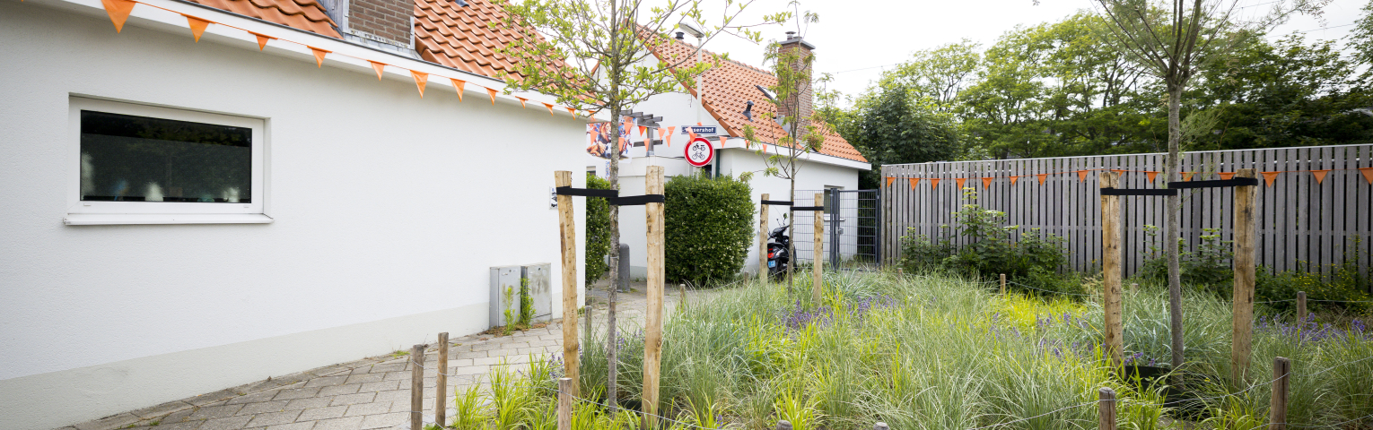 Een huis op Scheveningen met een rood dak en een groene tuin met bloemen.