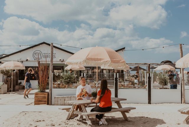 Houten en rieten meubels, jaren 70 parasols op het strand, kortom bij Beachclub Birds beleef je een echte strandvibe.