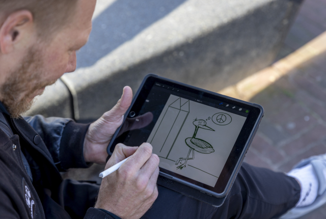 Merk ambassadeur Pat Smith krabbelt op een touchscreen een ooievaar en zijn denkbeeld van Vrede & Recht.