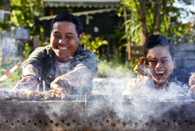 Twee mensen grillen lachend saté op barbecue