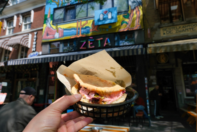 Een hand houdt een sandwich vast voor een kleurrijk restaurant